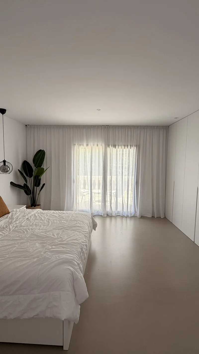 Dormitorio con cama blanca y visillos de lino frente a la terraza