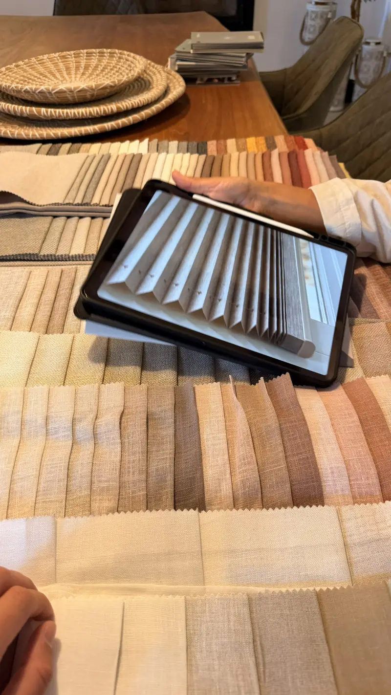 Muestras de tejidos en tonos naturales junto a una tableta con el plano de la casa