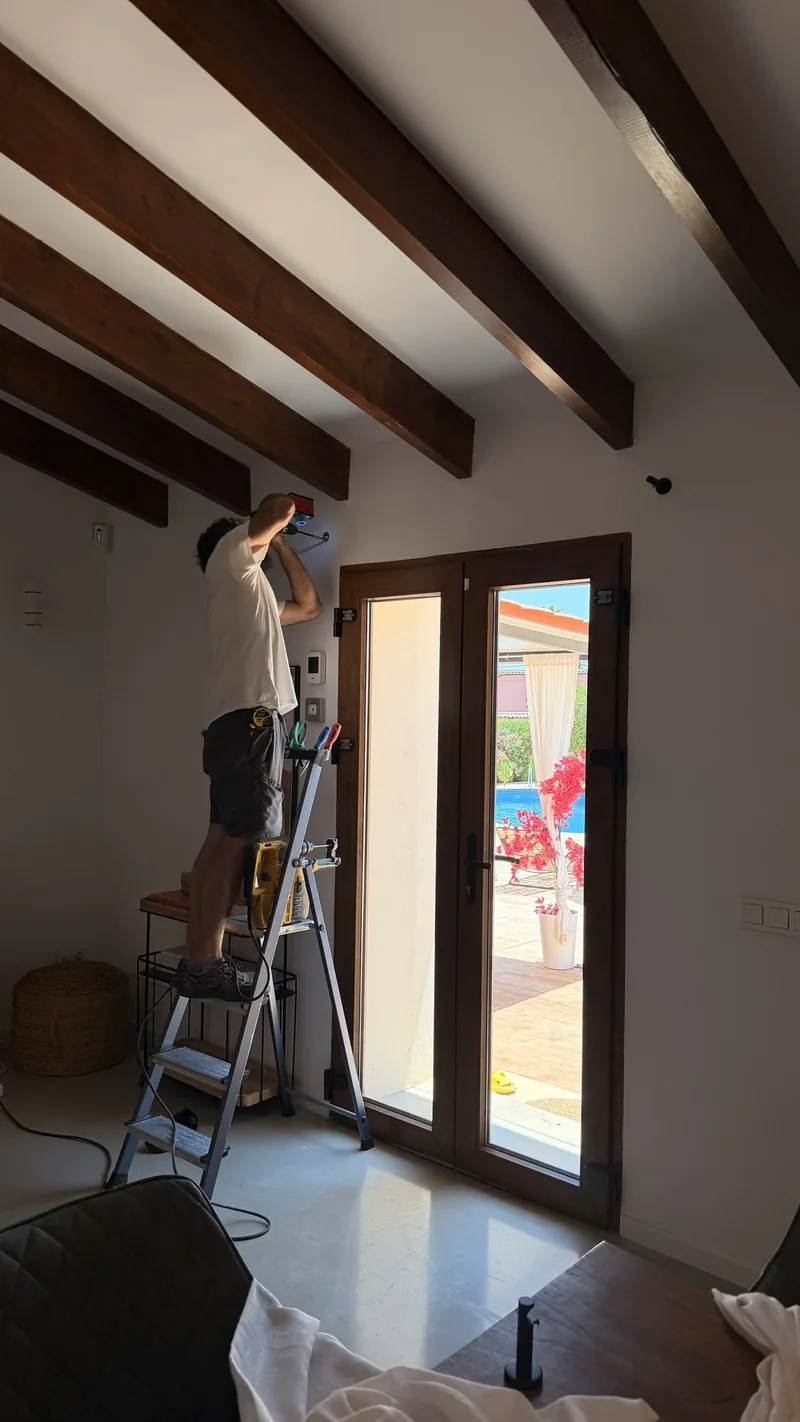 Instalador en una escalera colgando cortinas bajo un techo de vigas