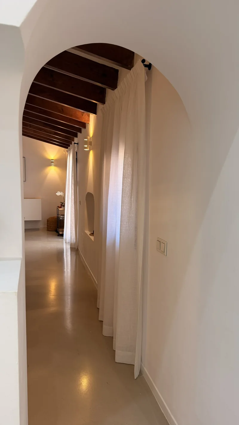 Pasillo con arco y techo de vigas de madera vestido con visillos blancos de lino