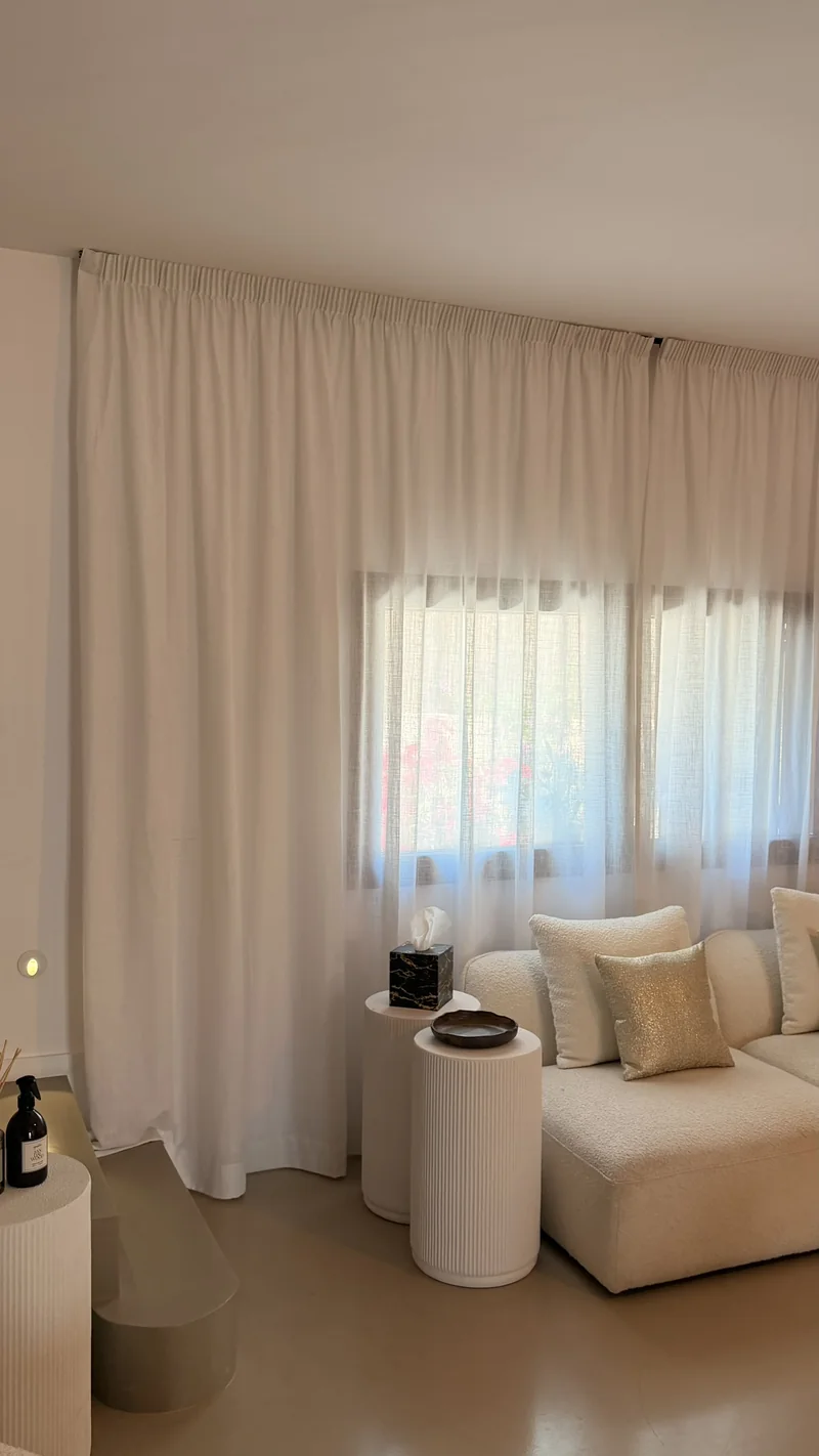 Salón con sofá blanco y visillos blancos de lino de suelo a techo