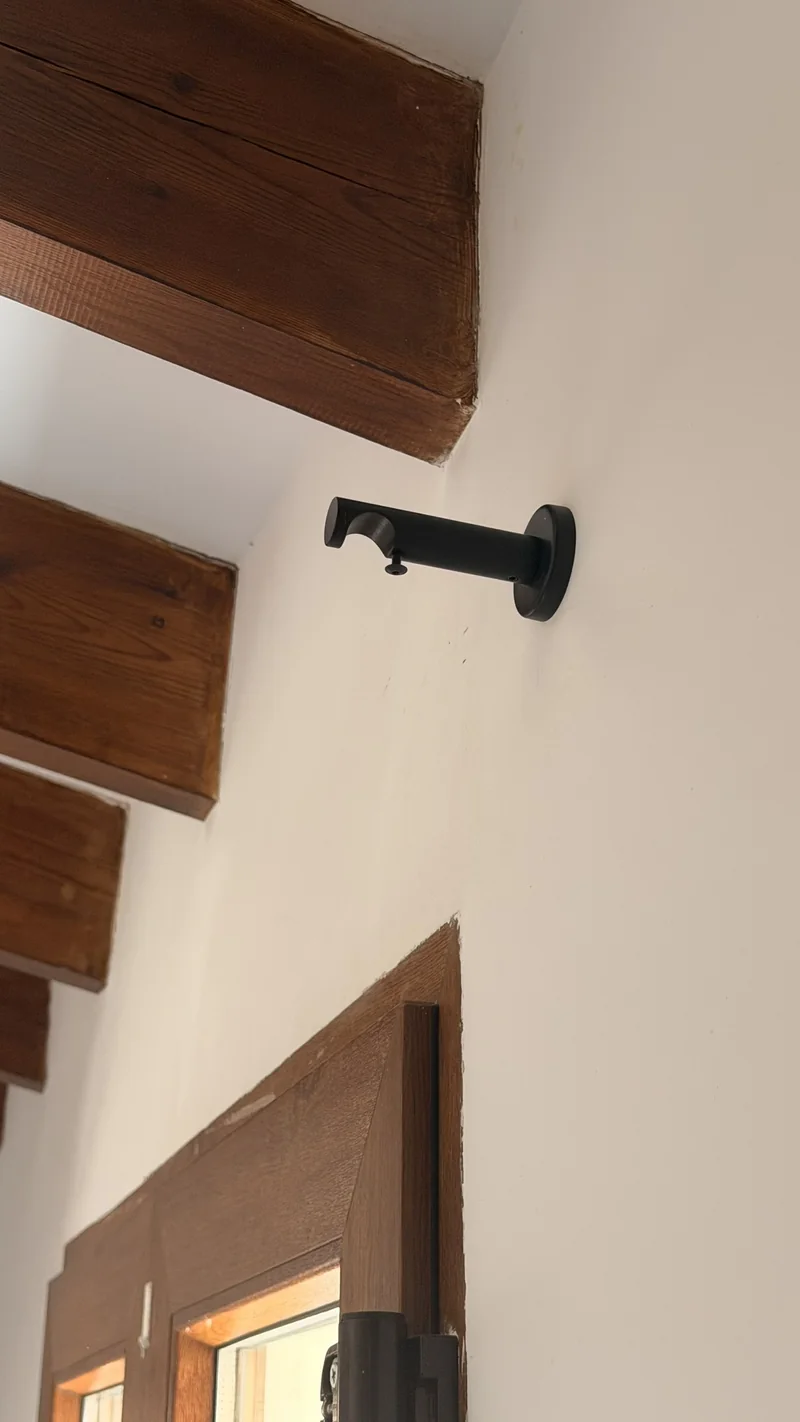 Soporte negro de barra de cortina fijado a la pared junto a una viga de madera