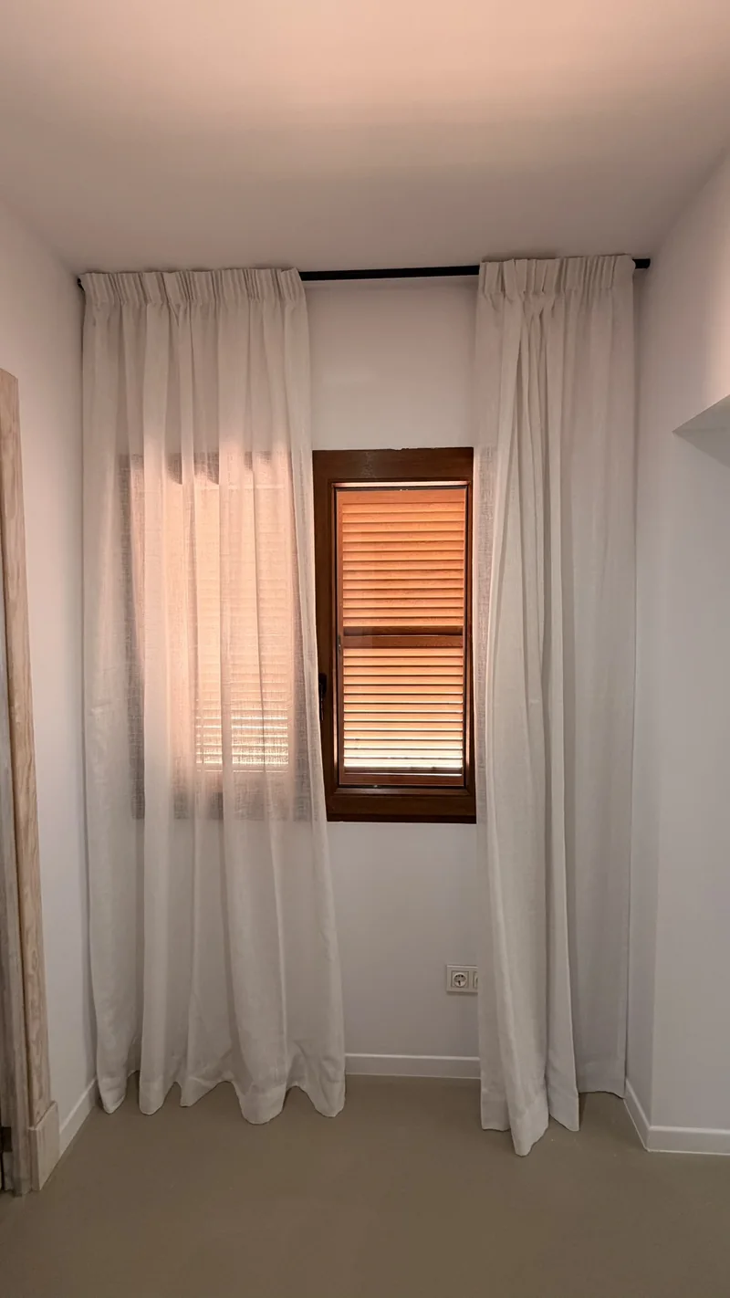 Visillos blancos a ambos lados de una ventana con contraventanas de madera