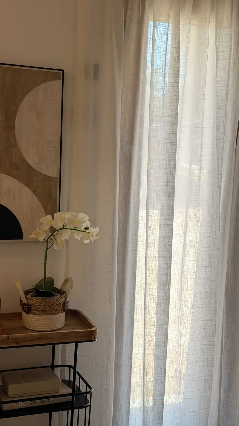 Visillo blanco de lino junto a una orquídea y un cuadro en tonos tierra