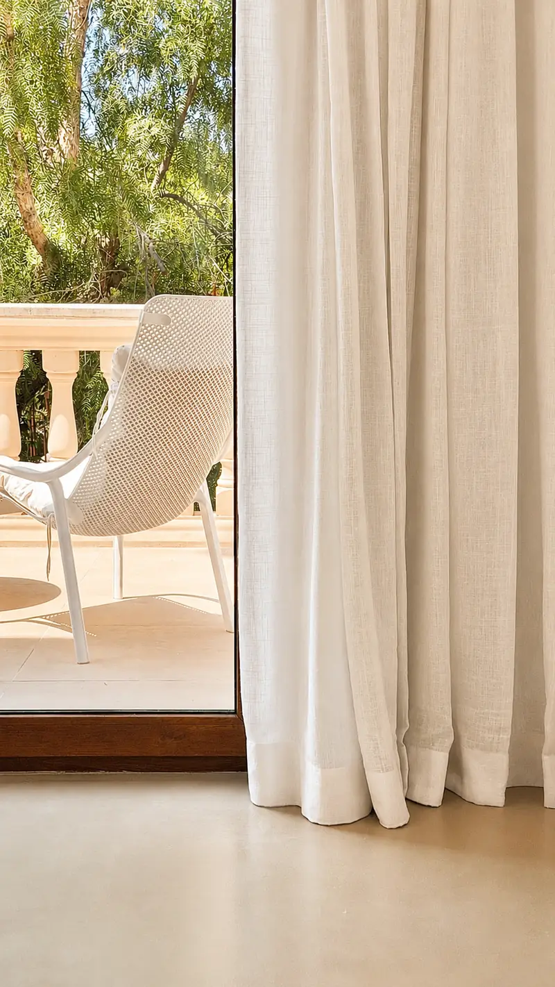 Visillo blanco de lino junto a la puerta de la terraza con una butaca blanca