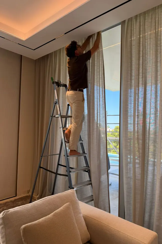Instalando cortinas de suelo a techo desde una escalera en un salón