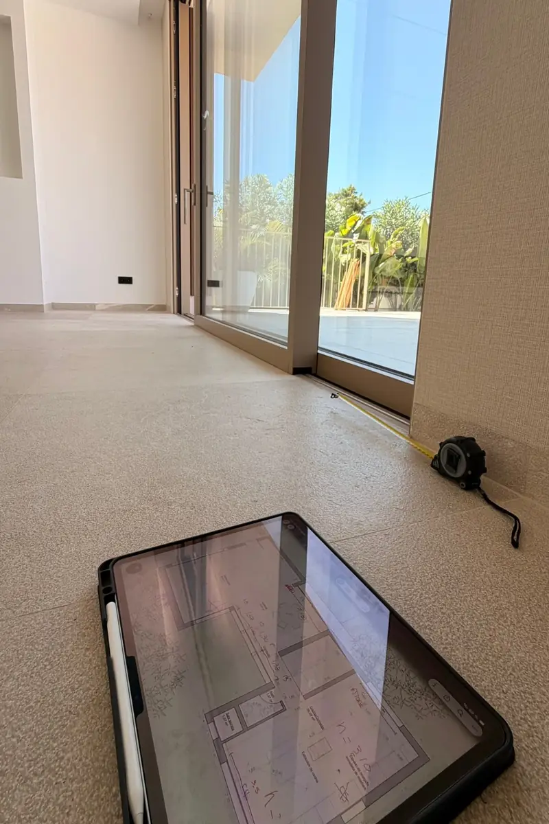 Medición del ventanal en obra con cinta métrica y el plano acotado en una tableta