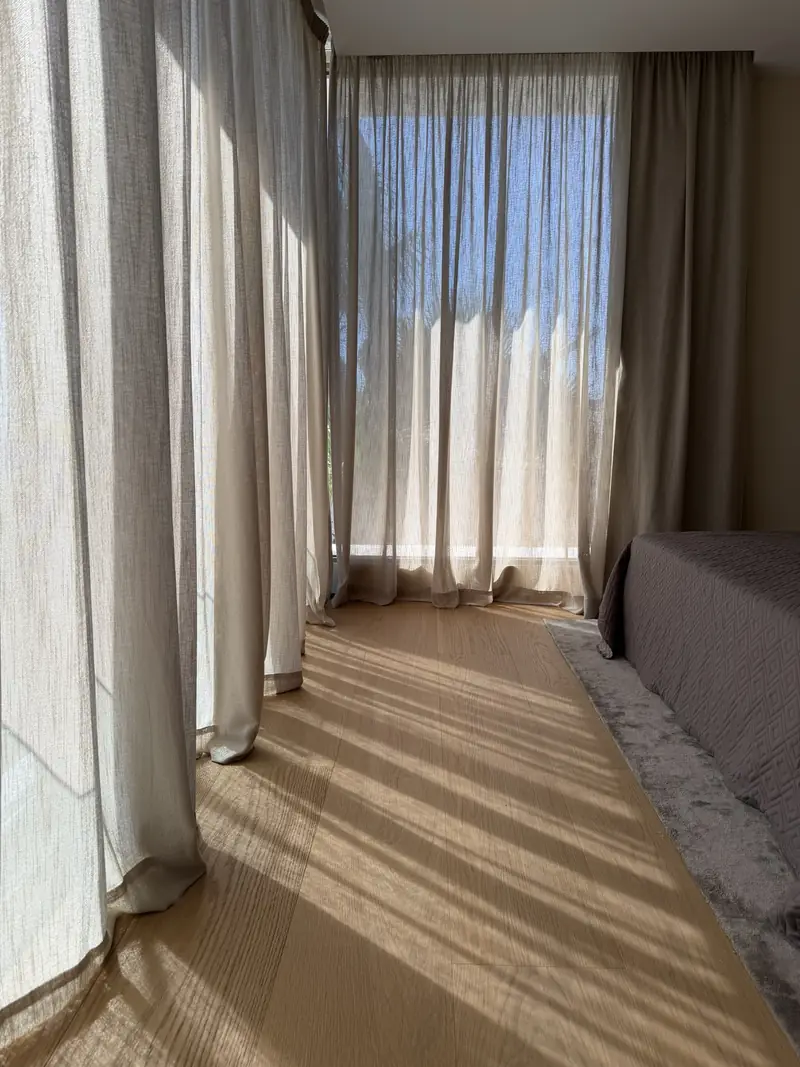 Visillo del dormitorio a contraluz dibujando franjas de luz sobre el suelo de madera