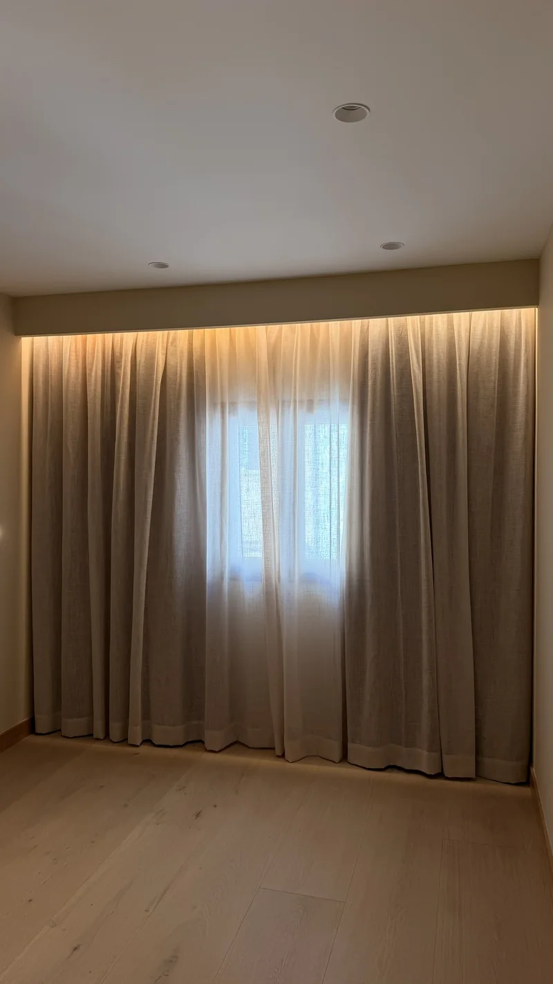 Dormitorio con cortinas de pared a pared bajo un foseado iluminado