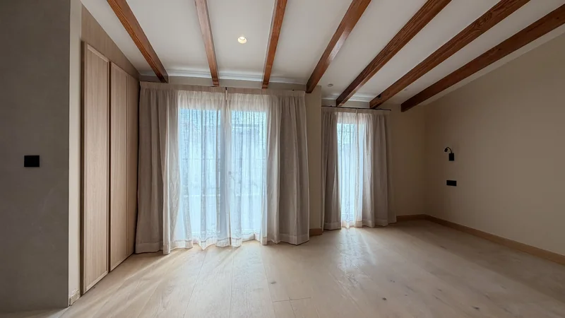 Dormitorio con vigas vistas y cortinas de lino en mezcla en una reforma junto al Pueblo Español, Palma