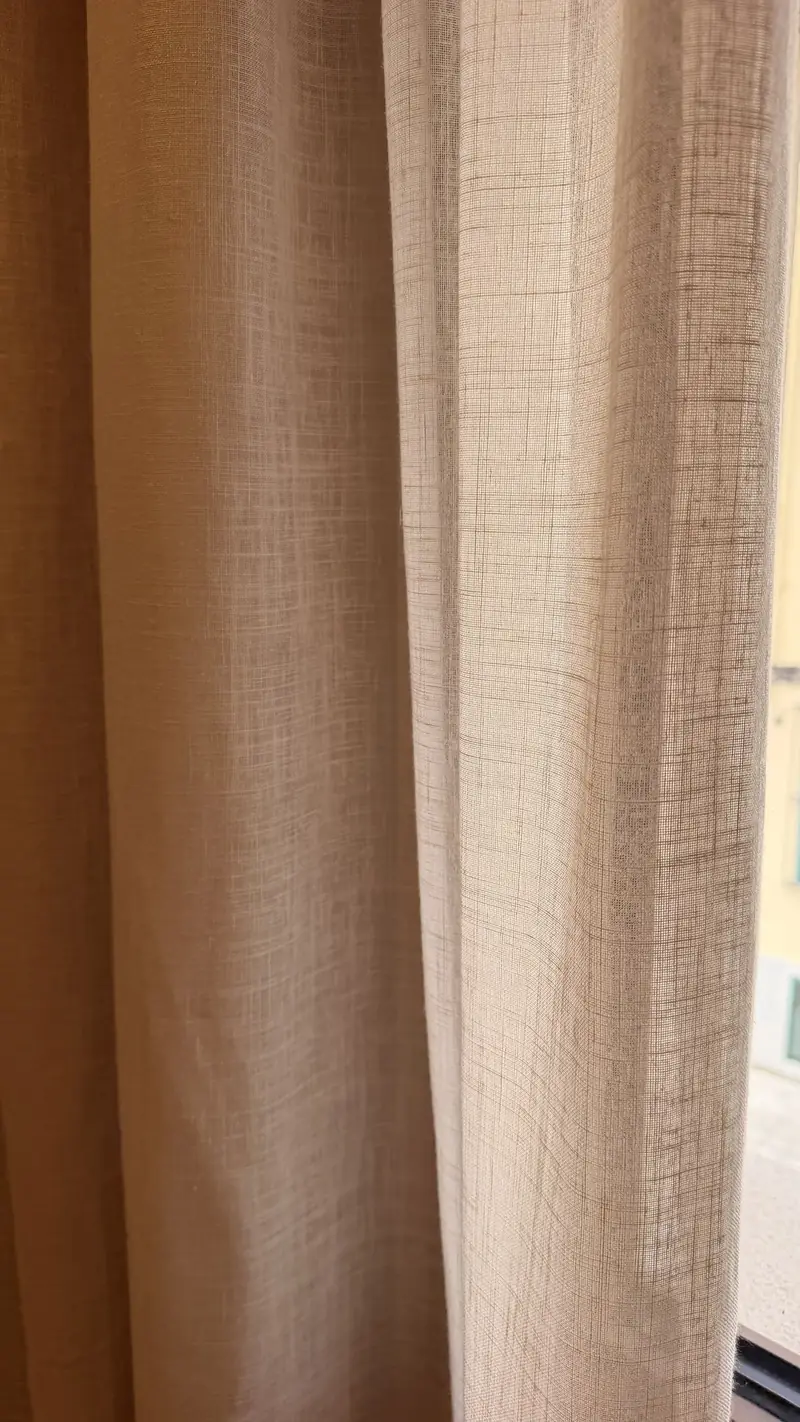 Detalle de la caída de una cortina en tono arena junto a la ventana
