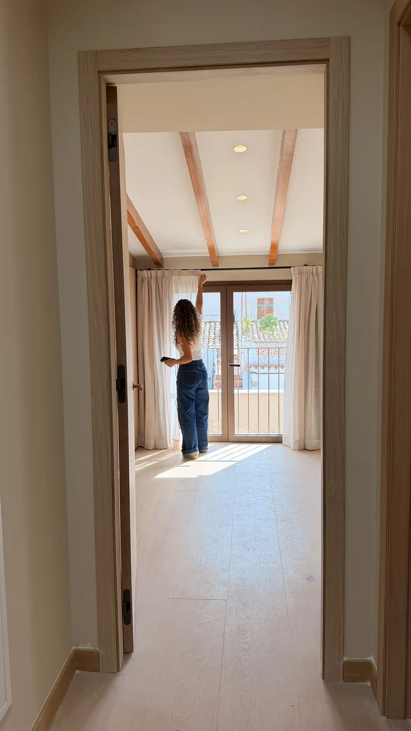 Vista desde la puerta de un dormitorio con vigas hacia el ventanal con visillo