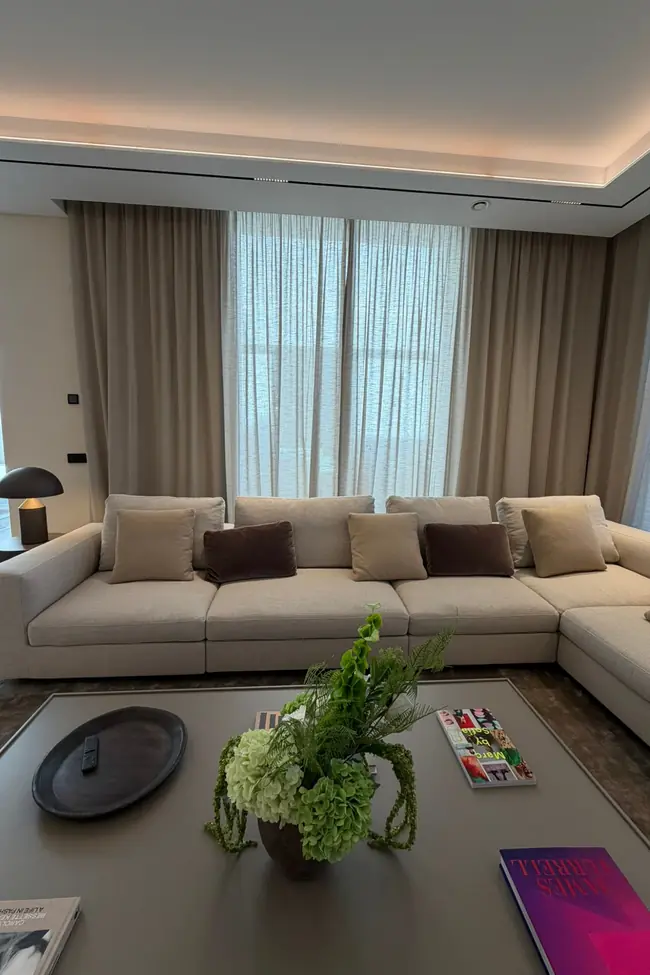 Salón con cortinas a medida en tono arena y visillos detrás del sofá